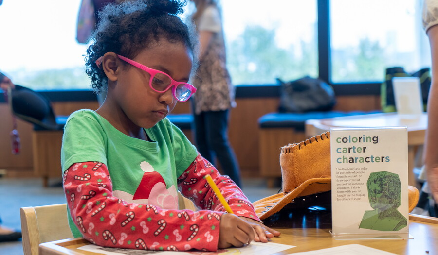 A child at a table draws on paper in the Carter's Family Pop-Up Space.