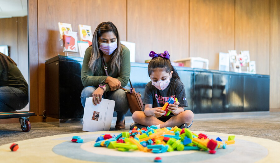 An adult and a child sit on the floor in the Carter Family Pop-up Space playing with colorful blocks.