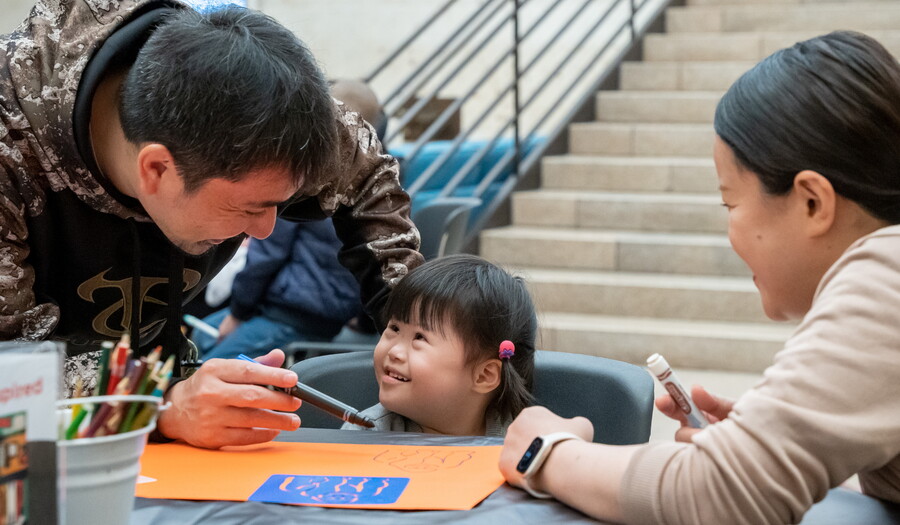 A toddler smiles at the adults helping her with an art project at the Carter.