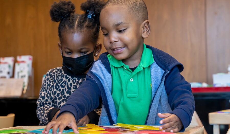 Two small children play with pieces of paper at a table in the Carter&#039;s Family Pop-up Space.