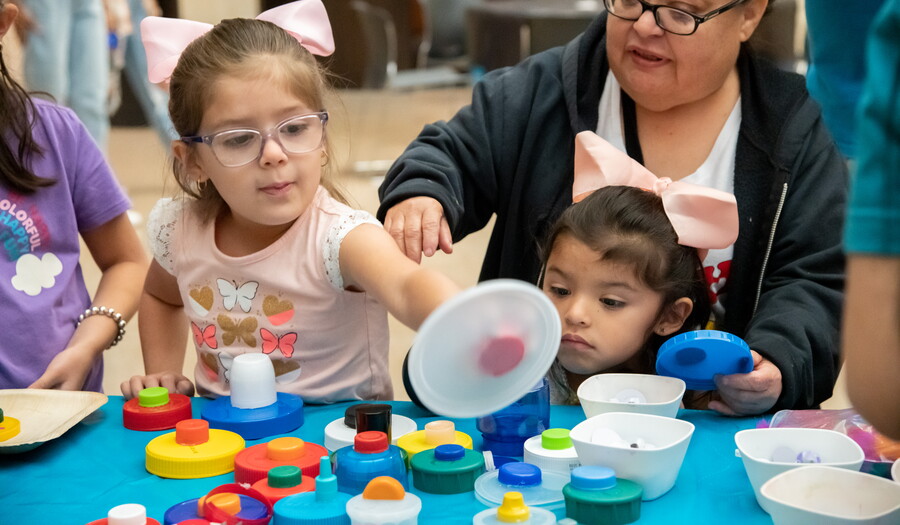 Children make art using colored plastics at a table in the Carter&#039;s Atrium.