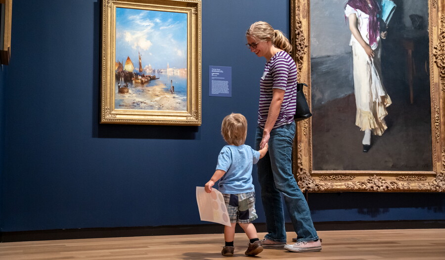 An adult woman holds the hand of a child as they look at art in a Carter gallery.