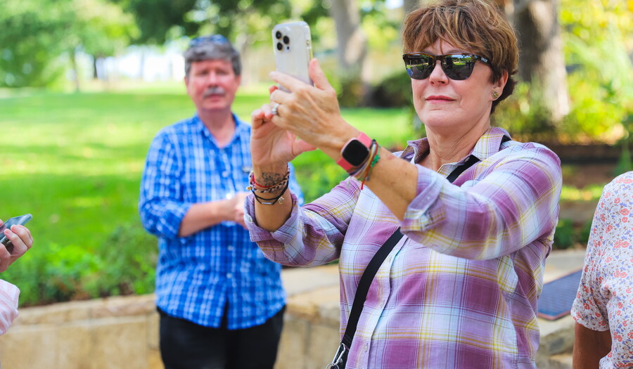A middle-aged White woman takes a photo of something with her phone.