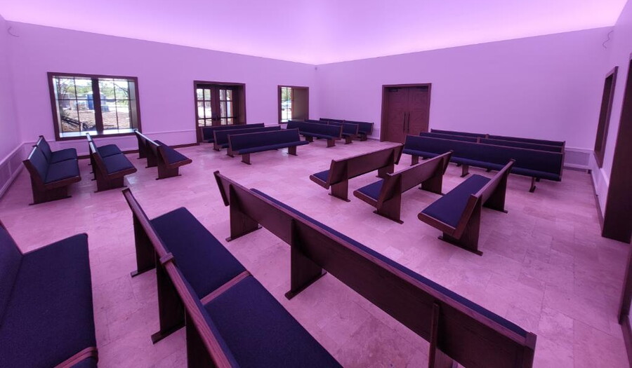 A large room filled with rows of church pews and bathed in a purple light.