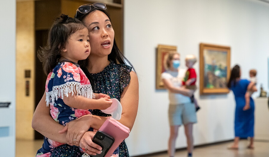 A woman and a young child she is holding on her hip look at art in a Carter gallery.