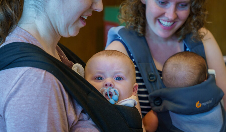 Two adults holding babies in carriers in a Carter gallery.