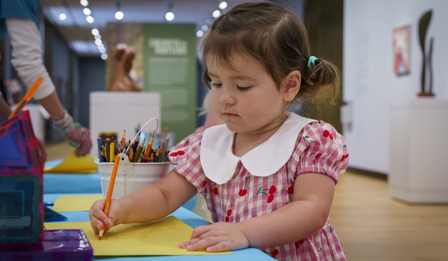 A child draws on a sheet of paper at a table in a Carter gallery.
