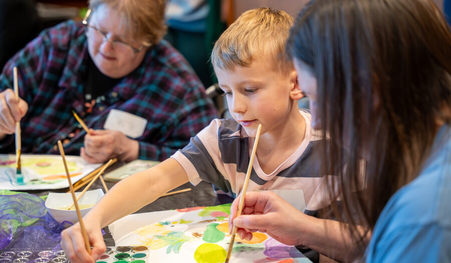 Two adults and a child, all White, painting watercolors at a table in the Carter&#039;s Pop-up Lounge.