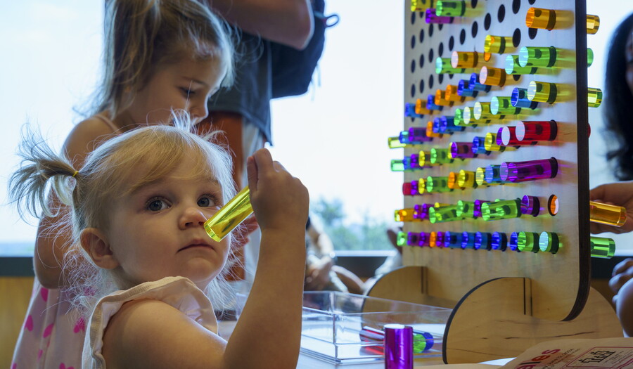 A young White child places colored pegs into a pegboard in a Carter gallery.