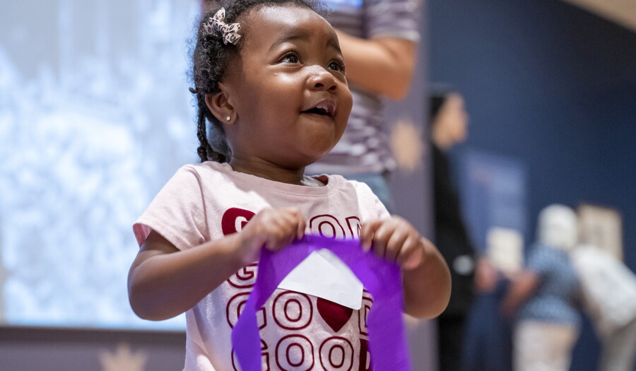 A black child smiles as she holds a purple streamer in a Carter gallery.