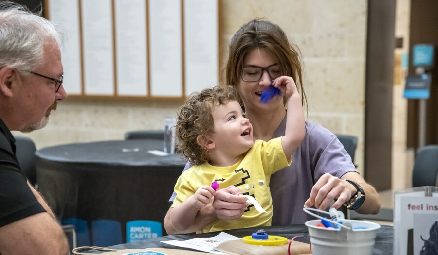 A White child sits on the lap of a woman as they laugh and make art at a table in the Carter's Atrium.