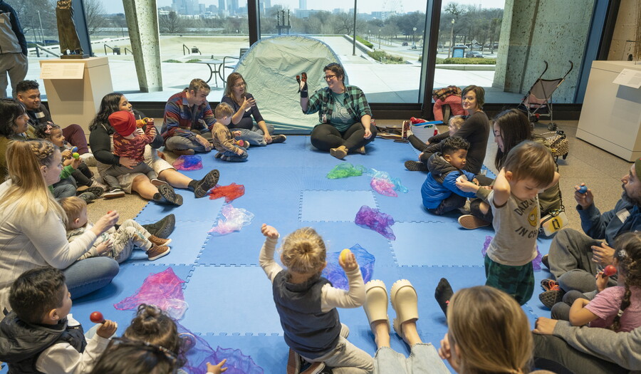A group of adults and children are seated on the floor of a Carter gallery around an educator.