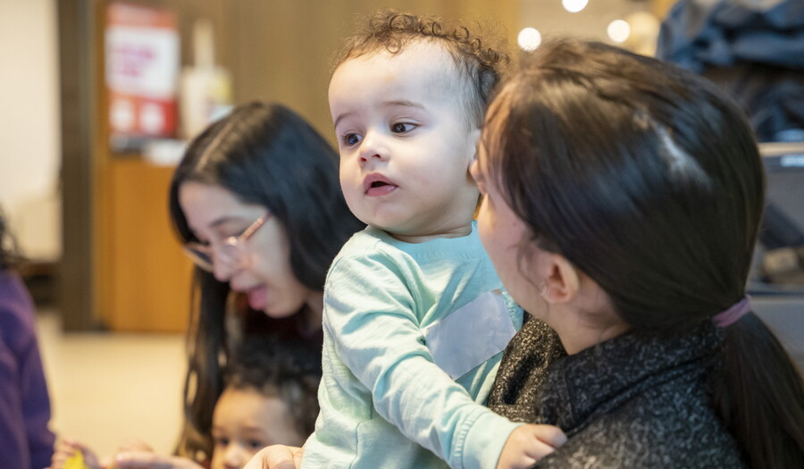 An adult holds a White baby with curly hair as they play in the Carter&#039;s Family Pop-up Space.