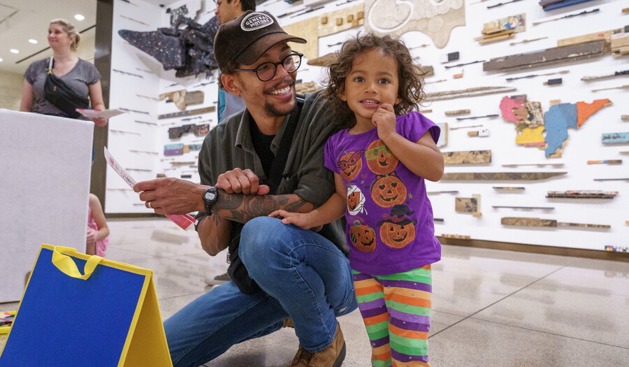 A medium-skinned man squats next to a medium-skinned child participating in an activity in a Carter gallery.