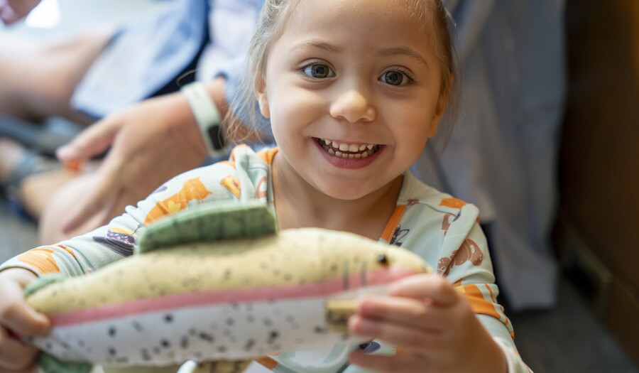 A close-up of a smiling child who is holding up a toy to see.