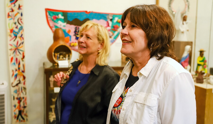 Two smiling White women look at art in an artist's studio.