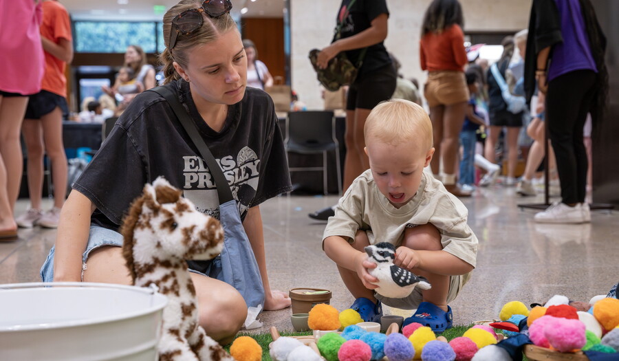 A White woman and small child on the floor of the Carter Atrium playing with colorful pompoms.