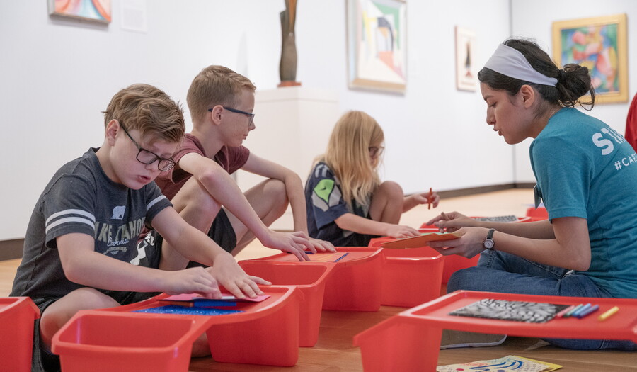 Three middle-school age children and a Carter educator sit on the floor of a gallery making art.