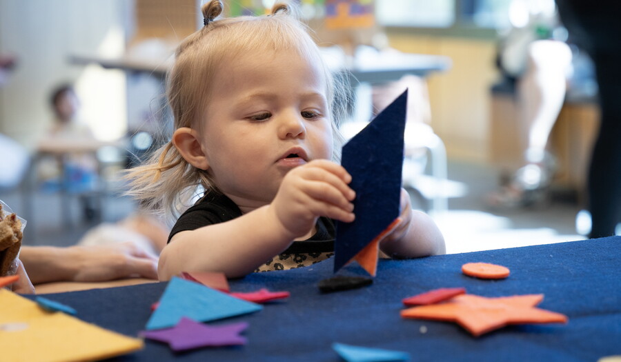 A small White child at a table playing with colored felt in the shapes of stars and triangles.