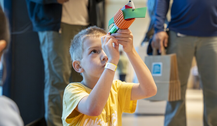 A White child looks in a tube made from colored construction paper in the Carter's Atrium.