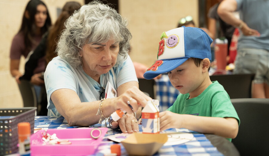 An older White woman helps a young White child make art at a table in the Carter's Atrium.