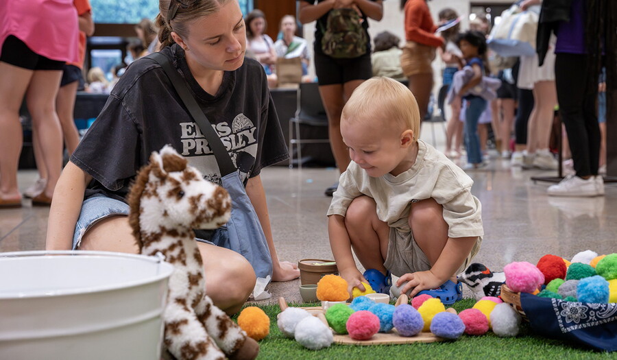 A small child plays with colorful pom-poms in the Carter's Atrium.
