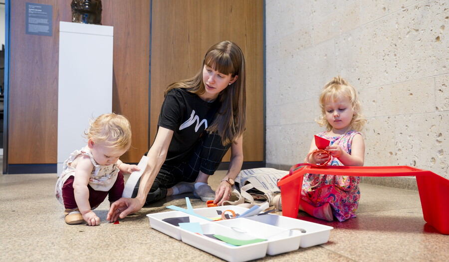 A White woman and two small children play with art supplies on the floor of a Carter gallery.