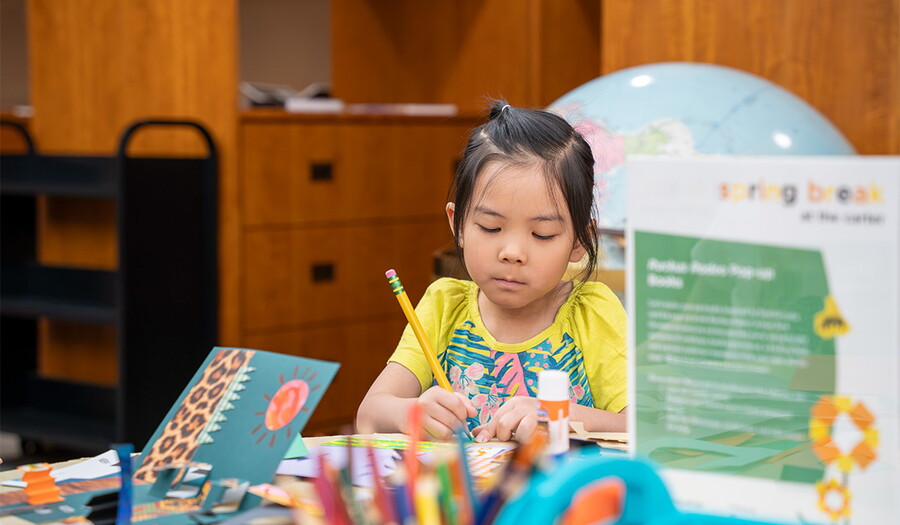 A young child with Asian features is focused on making art in the Carter's Library.