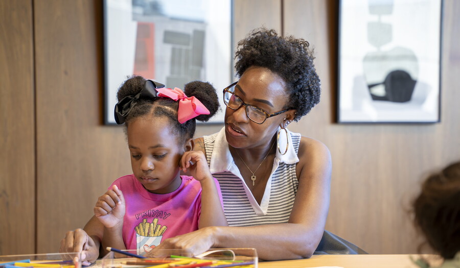 A Black woman and the child on her lap make art in the Carter's Family Pop-Up Space.
