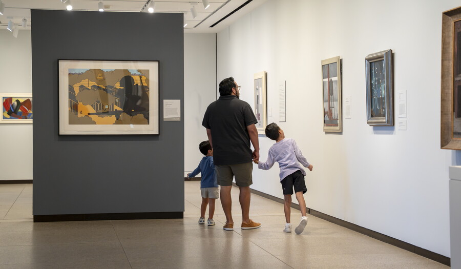 A White man holds hands with two small children as the look at art in the Carter galleries.