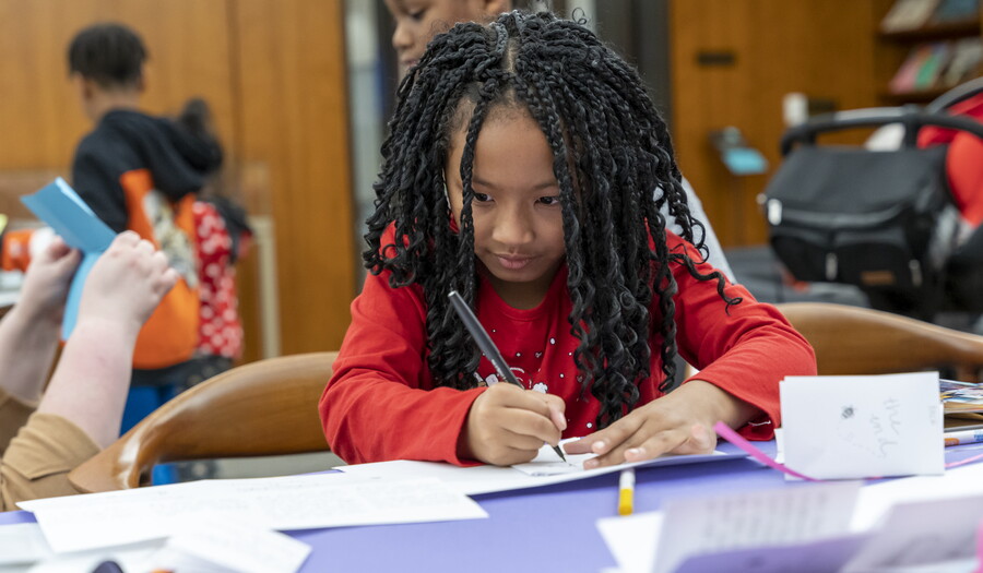 A dark-skinned child with long hair draws at a table in the Carter's Family Pop-up Space.