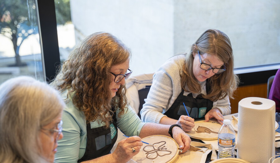 Three White women are seated at a table in the Carter's Lounge making art together.