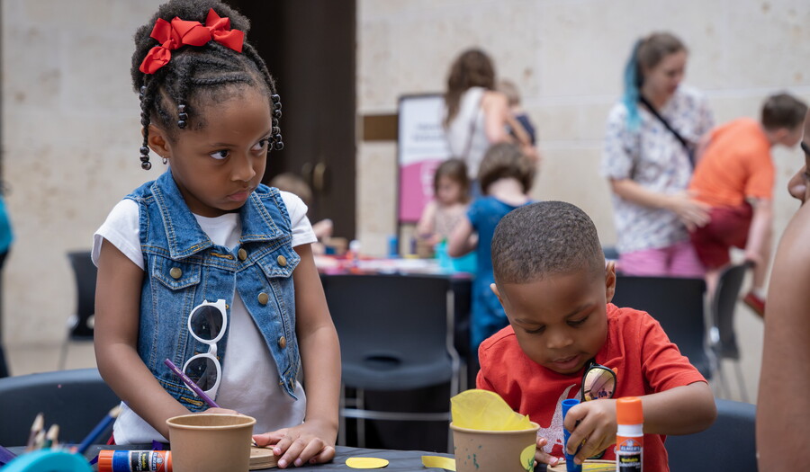 Two Black children use glue sticks and construction paper to make art in the Carter's Atrium.
