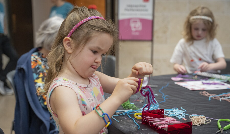 A young White child uses yarn and colored pipe cleaners to make art at a table in the Carter's Atrium,