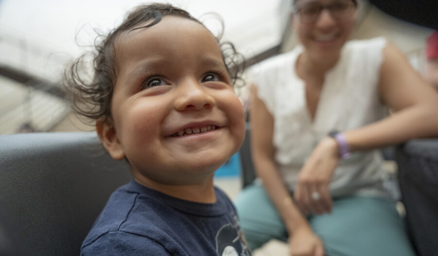 A smiling medium-skinned toddler-aged child plays in the Carter's Atrium.