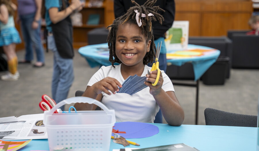 A smiling pre-teen Black girl makes art at a table in the Carter's Family Pop-up Space.