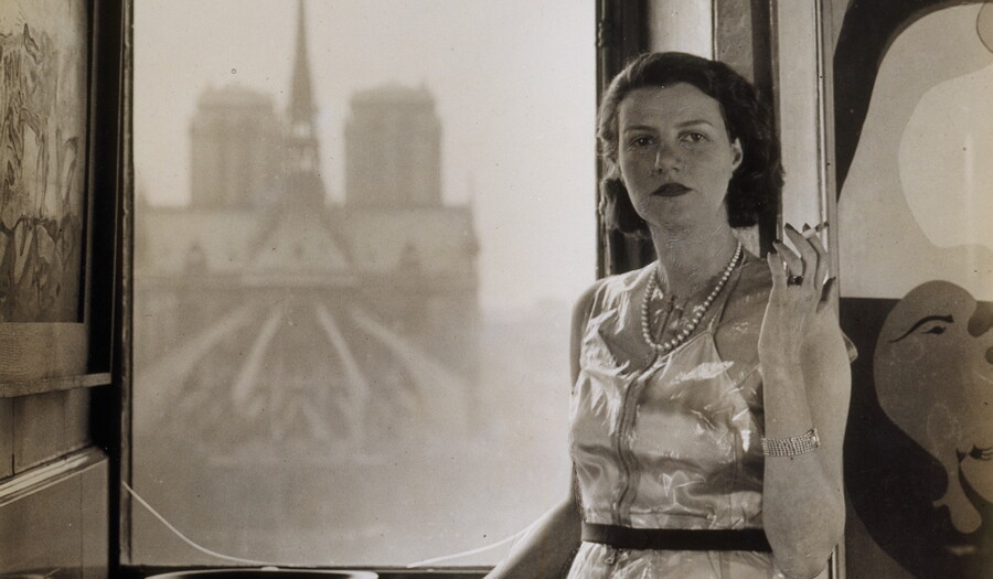 A black-and-white photograph of a young White woman standing in front of a window through which you can see the back of a church.