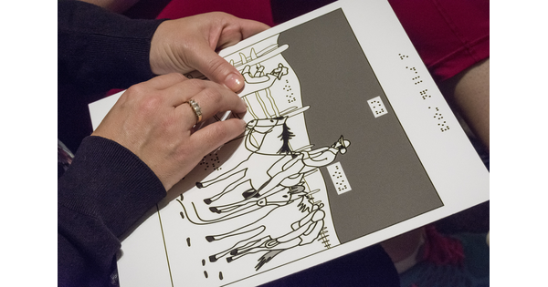 Close-up of hands exploring a raised-line drawing of an artwork.