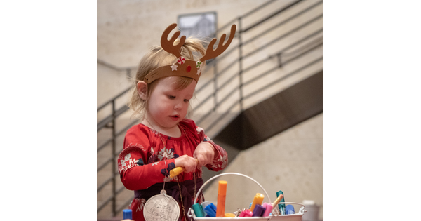 A toddlers wearing a headband with antlers on it makes art.