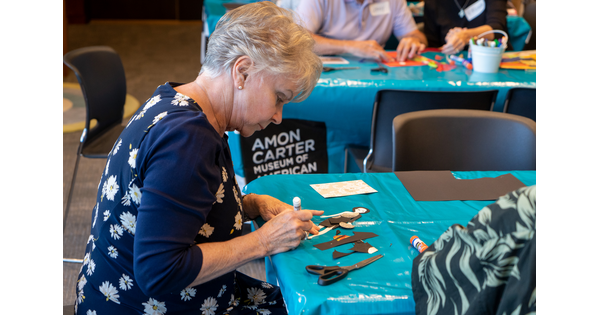A senior sits at a table and works on a craft.