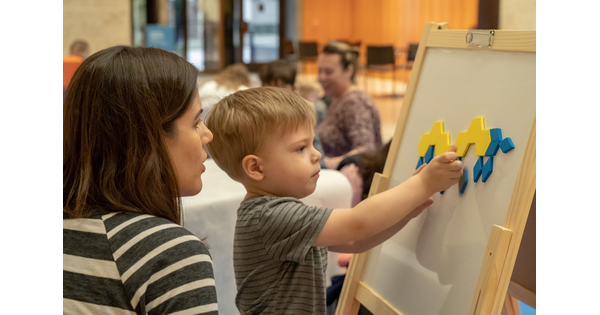An adult watches a toddler play with a magnet board.