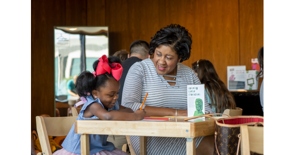 A toddler colors at a table while an adult watches.