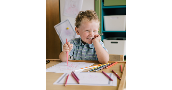 A toddler uses colored pencils to draw on paper.