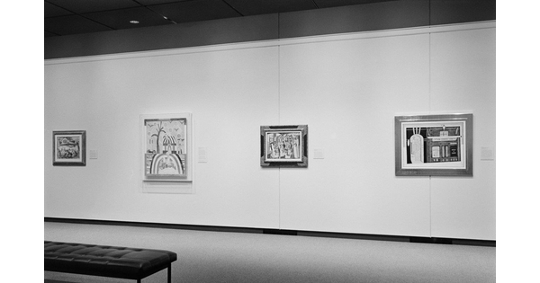 Black and white photo of installation showing four paintings hanging on a light wall. The second from left is Portrait Arrangement by Marsden Hartley.