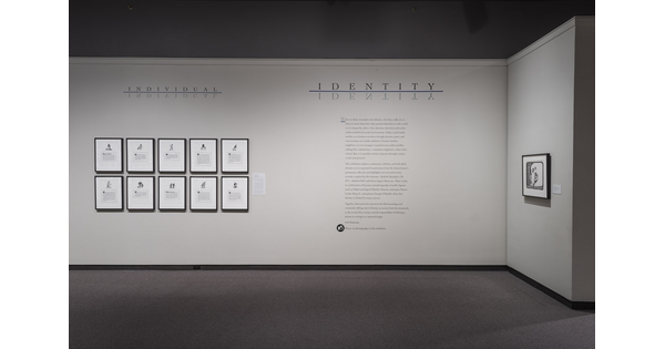 White wall with exhibition text to the right of 10 framed lithographs.