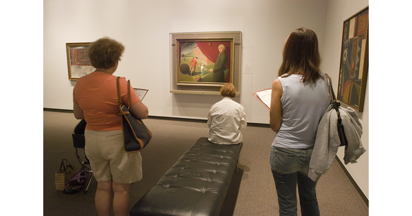 Three adults in a gallery look at a painting.