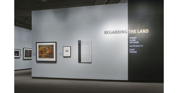 Title wall featuring an exhibition panel and two framed photographs. Beyond this wall, several other photos can be seen.