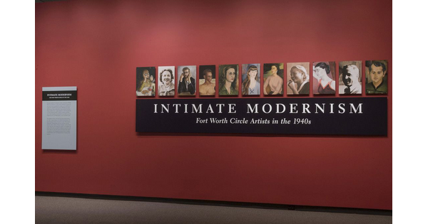 A red title wall with a black panel containing the exhibition title; above it are 11 panels featuring portraits of people.