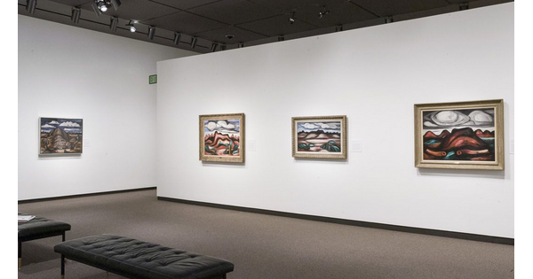 View of gallery with white walls; four framed abstract landscape paintings hang on the walls.