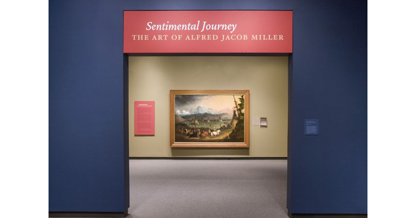 Entrance to gallery. Above the doorway is the title on a red background; through the doorway is a framed painting of a landscape.